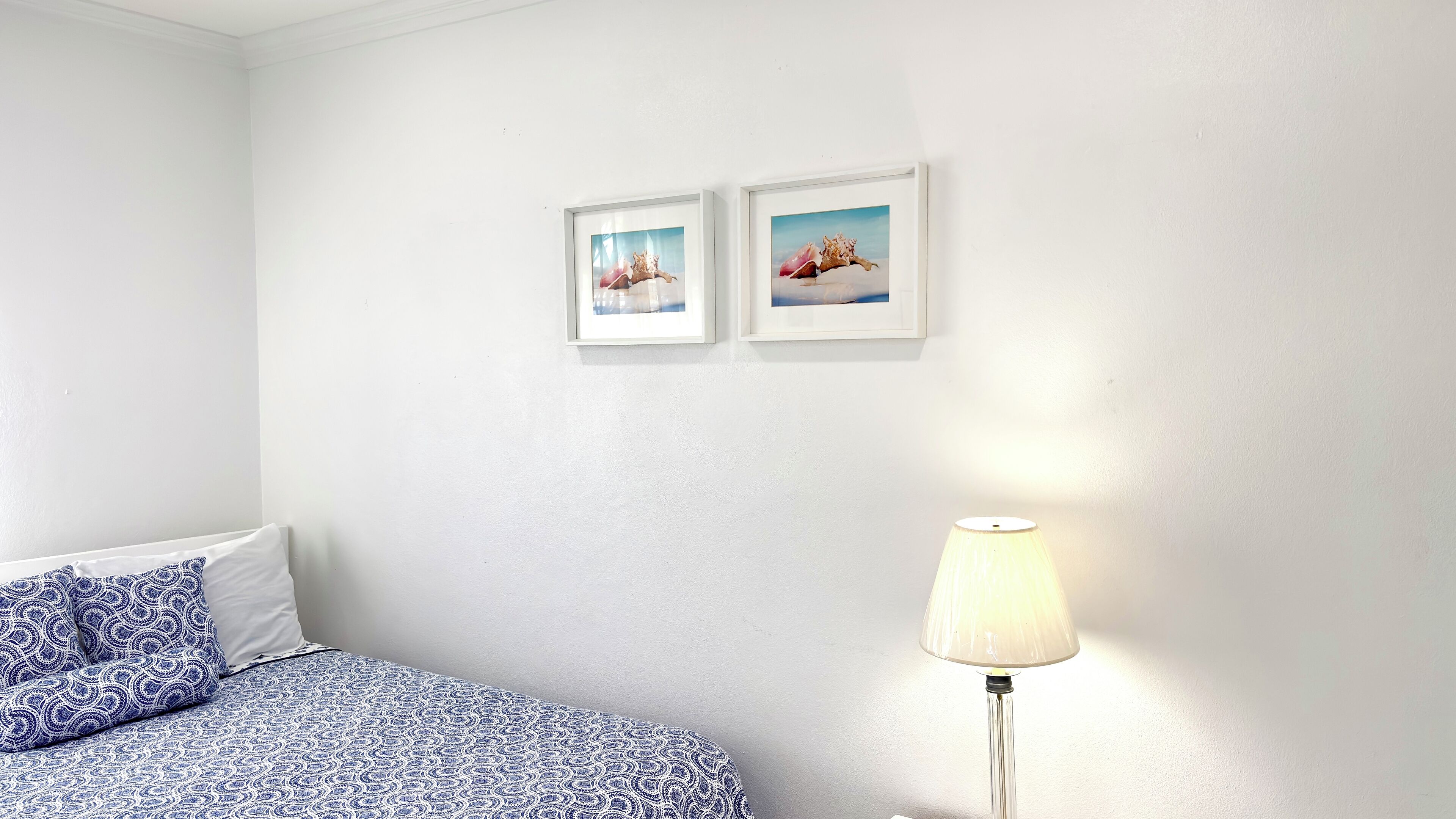 Une chambre à coucher avec un lit, deux tableaux encadrés au mur et une lampe de chevet.