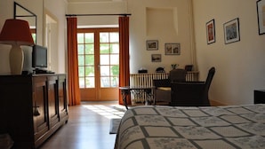 Un dormitorio con cama, escritorio, silla, radiador y ventana con cortinas.
