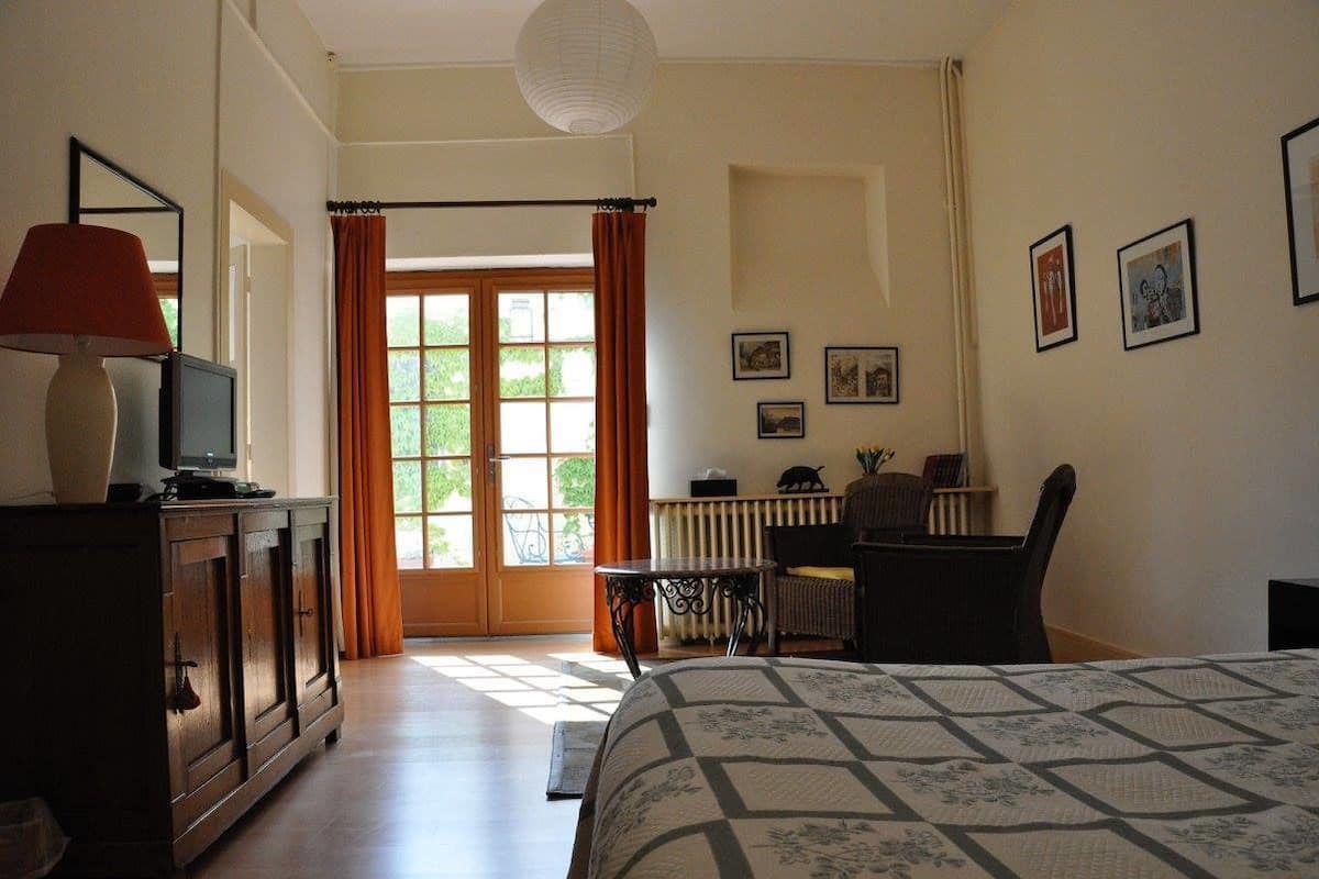 A bedroom with a bed, a desk, a chair, a radiator, and a window with curtains.