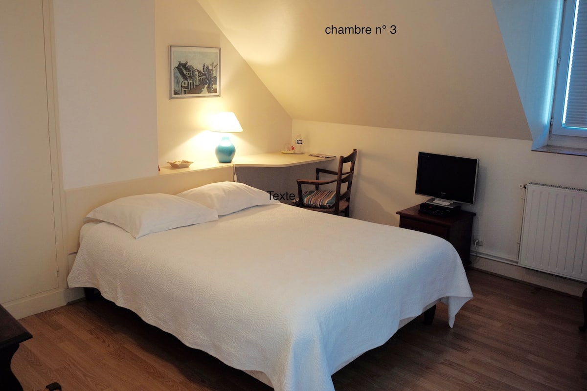 A bedroom with a bed, a desk, a chair, a TV, and a window.