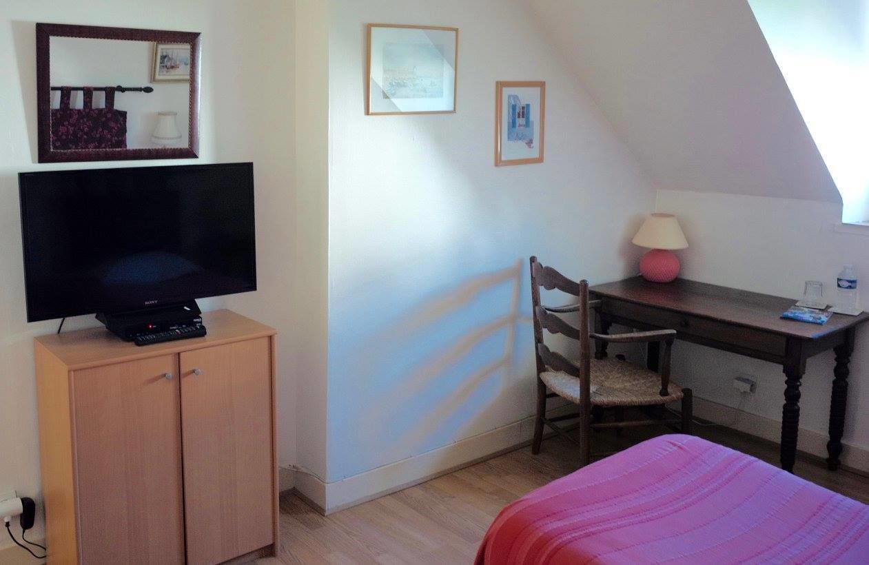 A small room with a bed, a desk, a chair, a TV on a cabinet, and framed pictures on the wall.