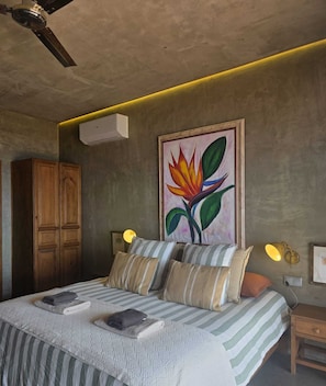 Un dormitorio con cama, almohadas, un cuadro, un armario y un equipo de aire acondicionado.