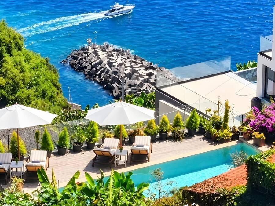 A rooftop pool with lounge chairs and umbrellas, overlooking a rocky shoreline and the sea.