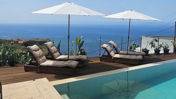 A pool area with lounge chairs and umbrellas, overlooking a clear blue ocean. - Les Terrasses Suites (Calheta)