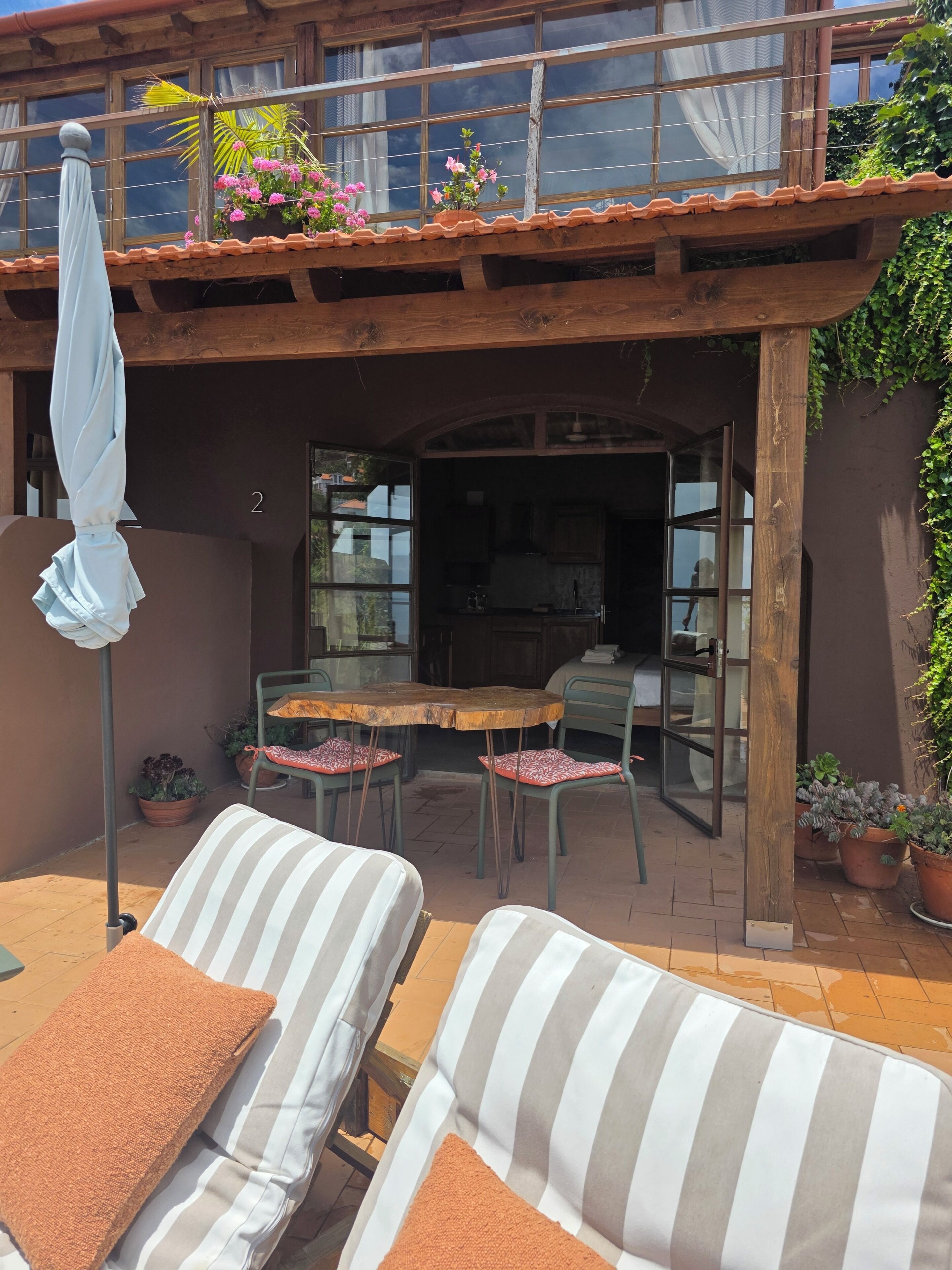 A patio area with a wooden table and chairs, a striped sofa, and a covered umbrella.