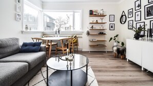 A modern living room with a grey sofa, a round glass coffee table, and a dining area with a wooden table and chairs. - Apartment V20 (Reykjavik)