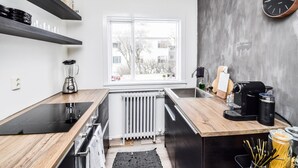 A modern kitchen with black countertops, a built-in stove, a coffee machine, and a window with a view of buildings. - Apartment V20 (Reykjavik)