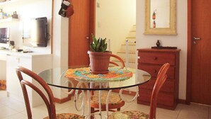 A dining area with a glass table surrounded by chairs, a potted plant, and a wooden cabinet with a mirror above it. - Duplex Caminho das Árvores (Salvador)