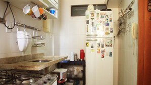 A compact kitchen with a gas stove, a refrigerator covered in magnets, and a coffee maker. - Duplex Caminho das Árvores (Salvador)