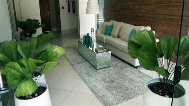 A modern living room with a sofa, coffee table, and large potted plants. - Duplex Caminho das Árvores (Salvador)