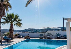 A pool area with lounge chairs, a palm tree, and a view of the landscape. - Villa Mina (Milos)