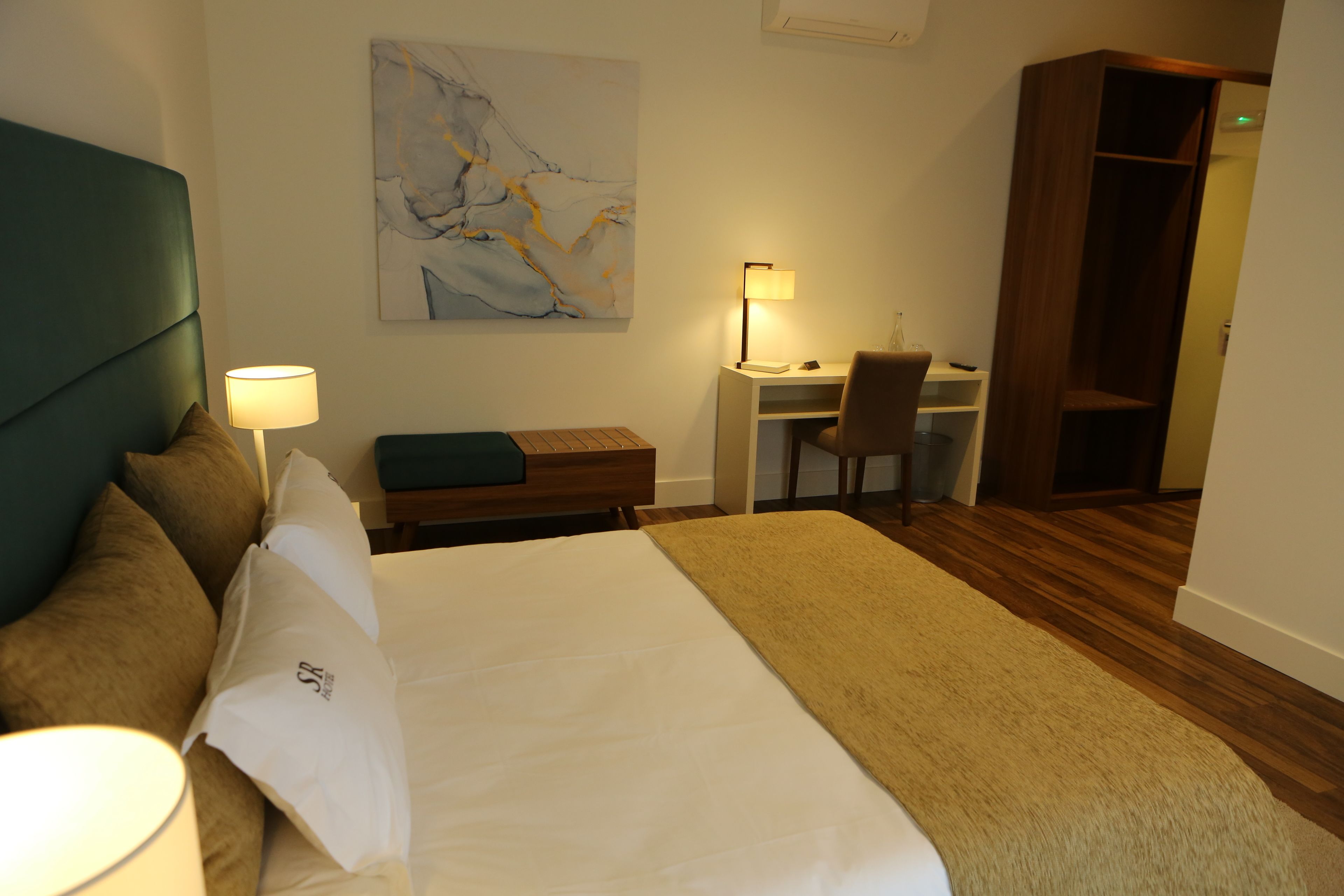 Habitación de hotel con cama, escritorio, silla, estantería y un cuadro en la pared.