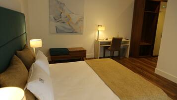 Habitación de hotel con cama, escritorio, silla, estantería y un cuadro en la pared.