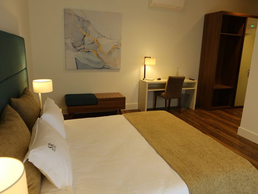 Habitación de hotel con cama, escritorio, silla, estantería y un cuadro en la pared.