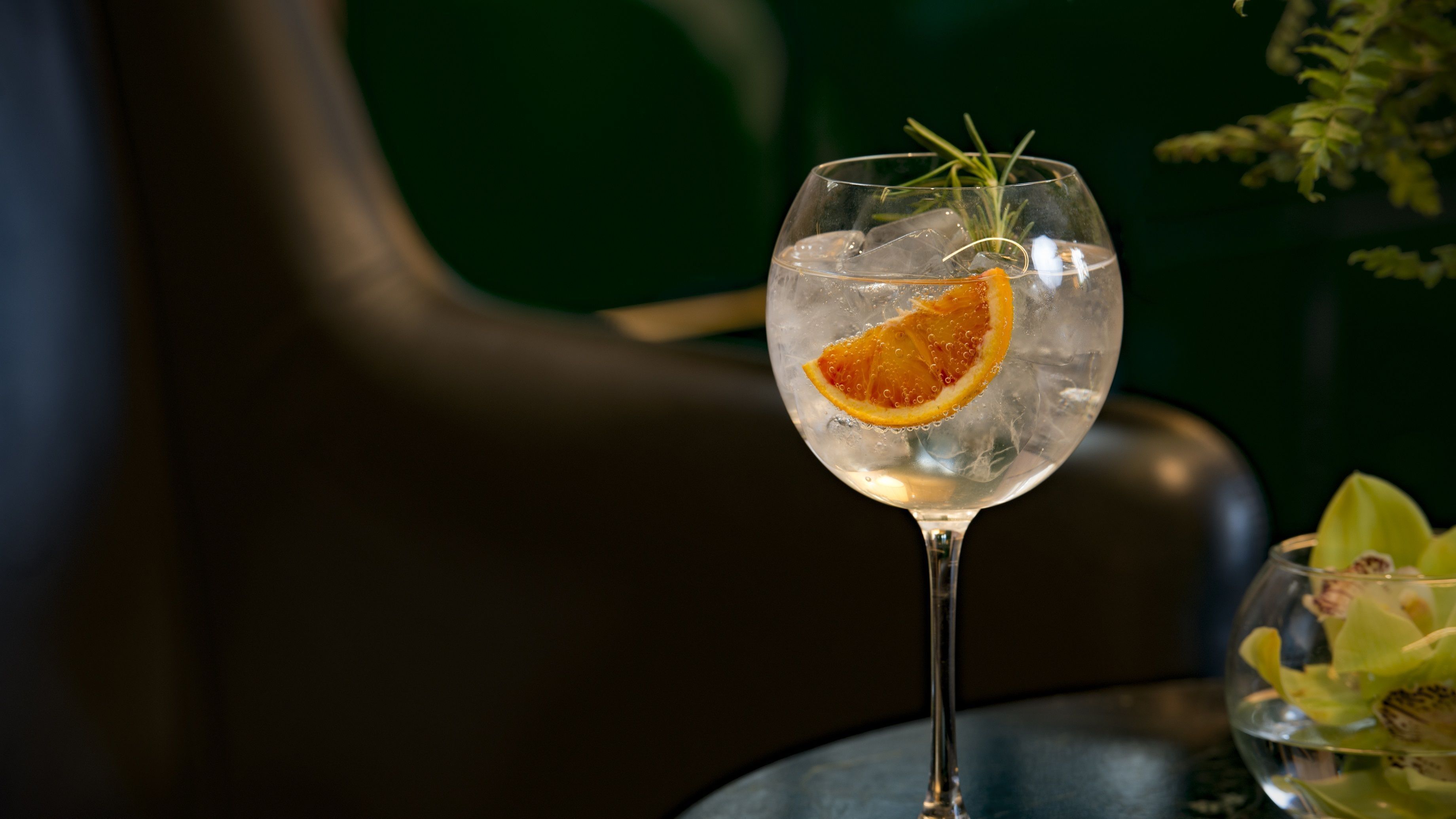 Un vaso transparente con hielo y una rodaja de naranja, sobre una mesa con fondo oscuro.