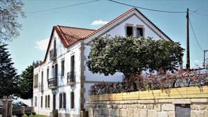 A white building with a red-tiled roof, a stone wall, and a large tree in front. - Hotel Solar do Rebolo (Oliveira do Hospital)
