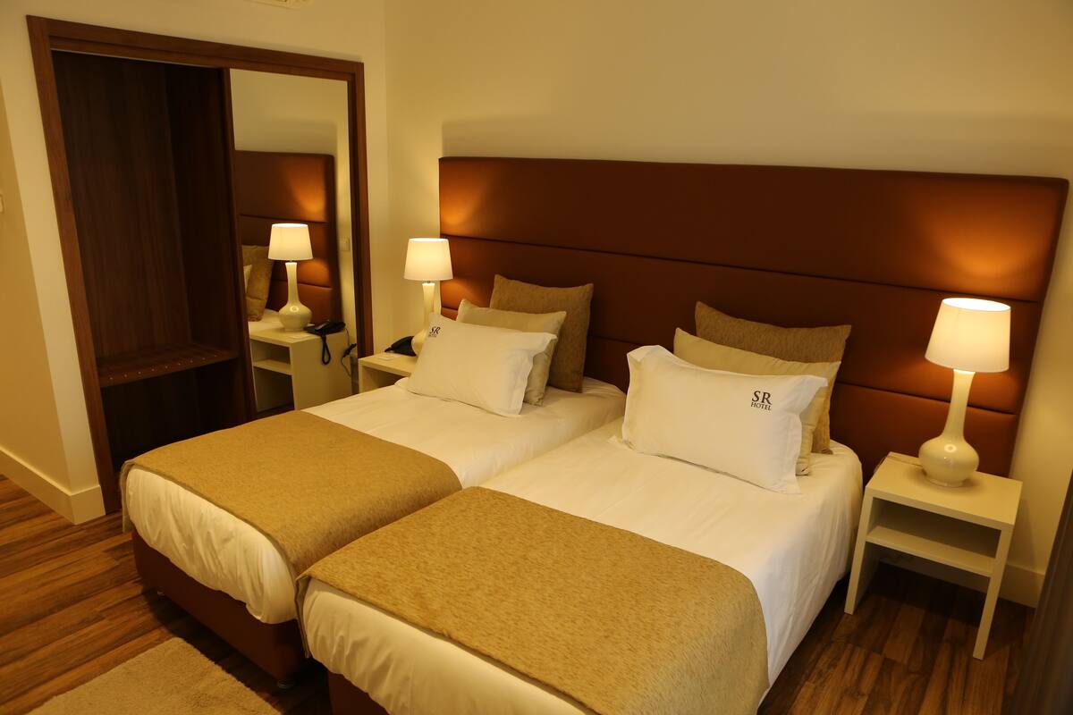A hotel room with two beds, a wooden headboard, bedside lamps, and a mirror.