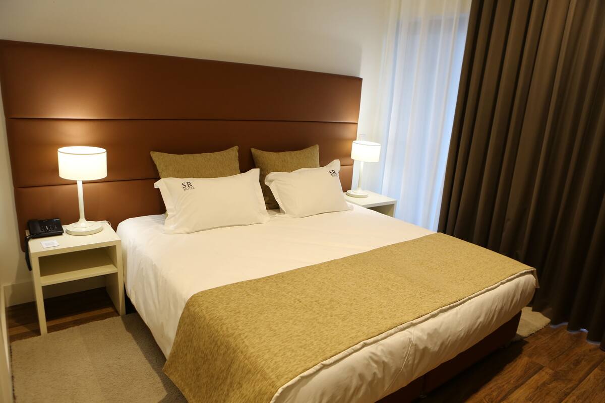 A hotel room with a large bed, two bedside tables with lamps, and a headboard.