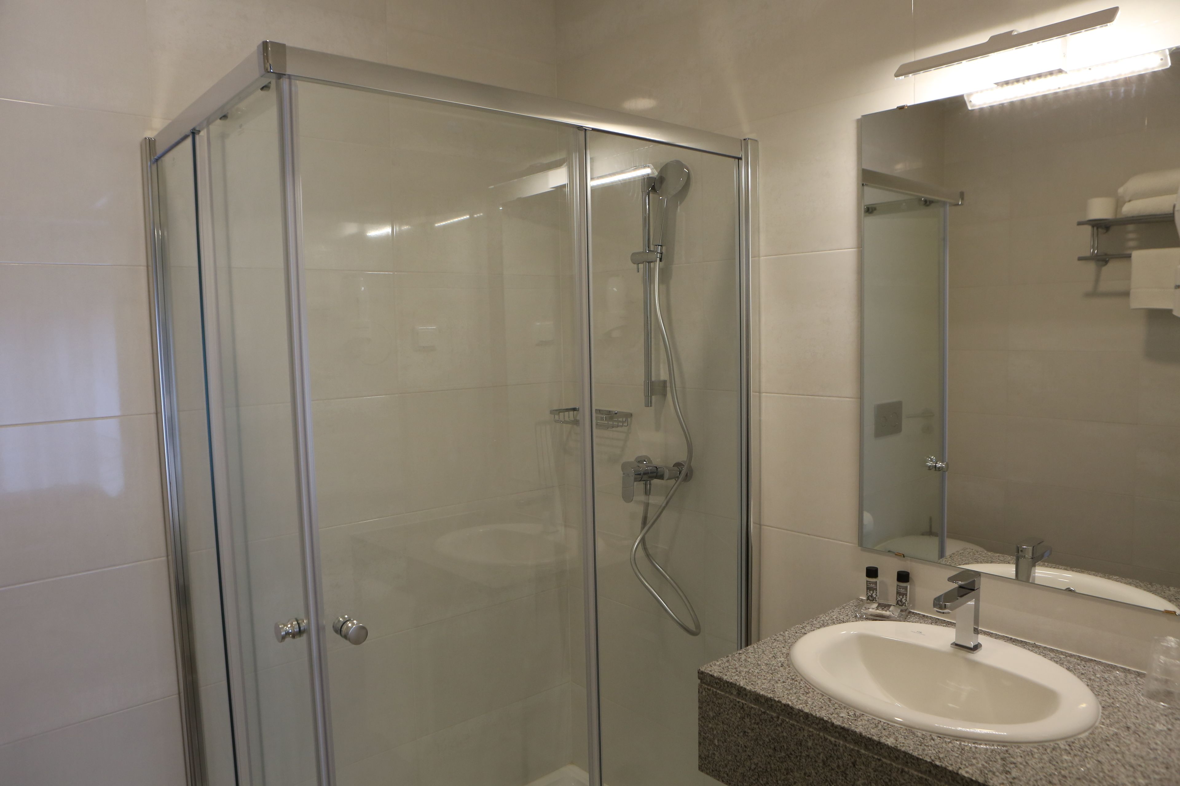 A modern bathroom with a glass-enclosed shower, a granite countertop sink, and a large mirror.