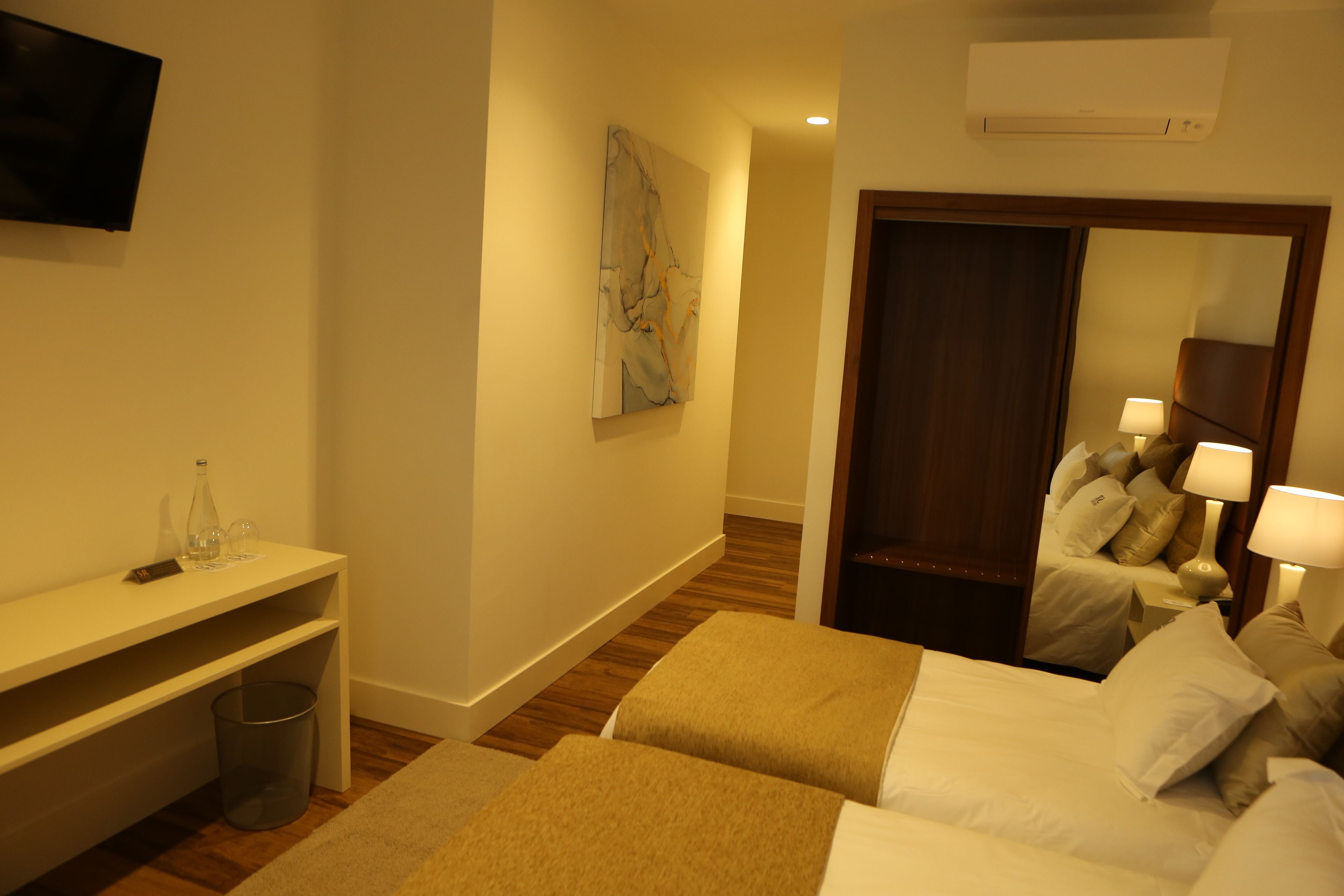 A hotel room with two beds, a desk, a television, a painting, and a mirror.