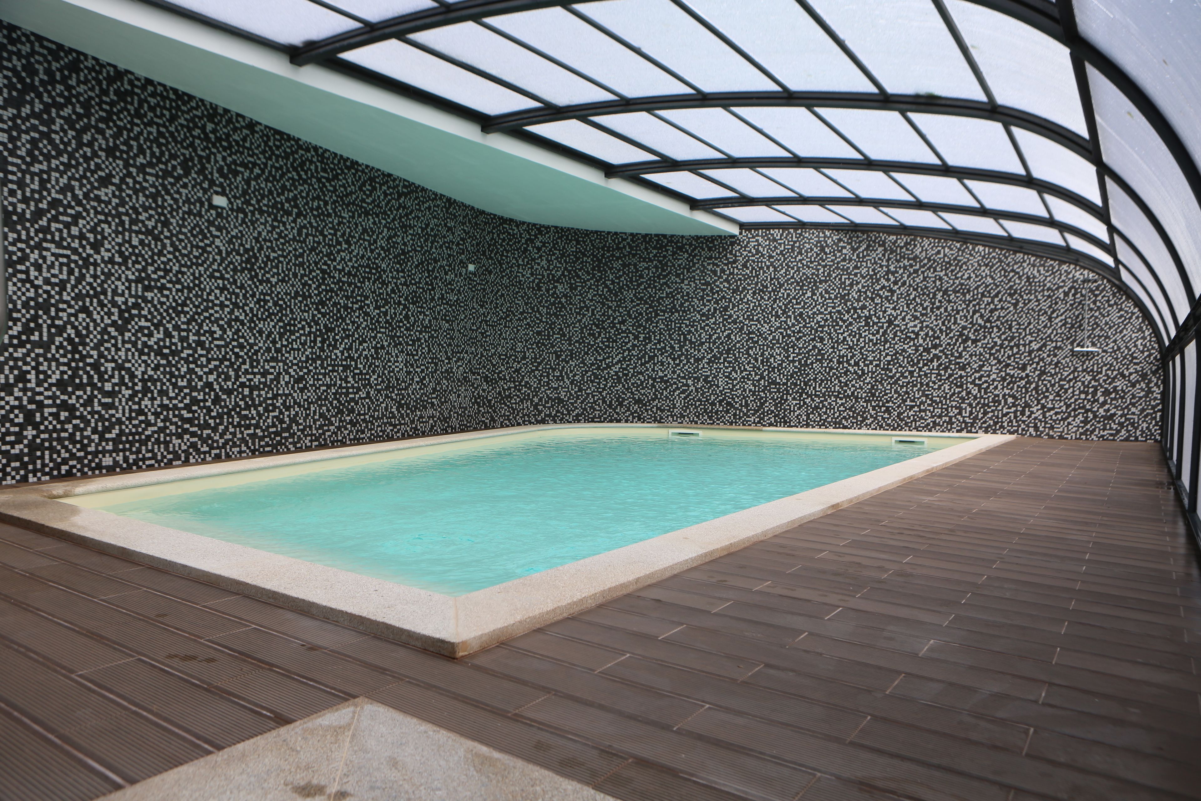 A swimming pool with a tiled wall and a wooden deck.