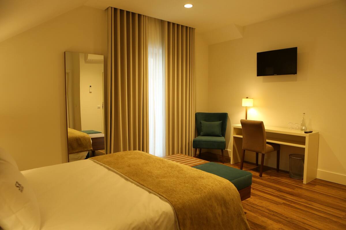 A hotel room with a bed, a desk with a chair, a television, and a window with curtains.