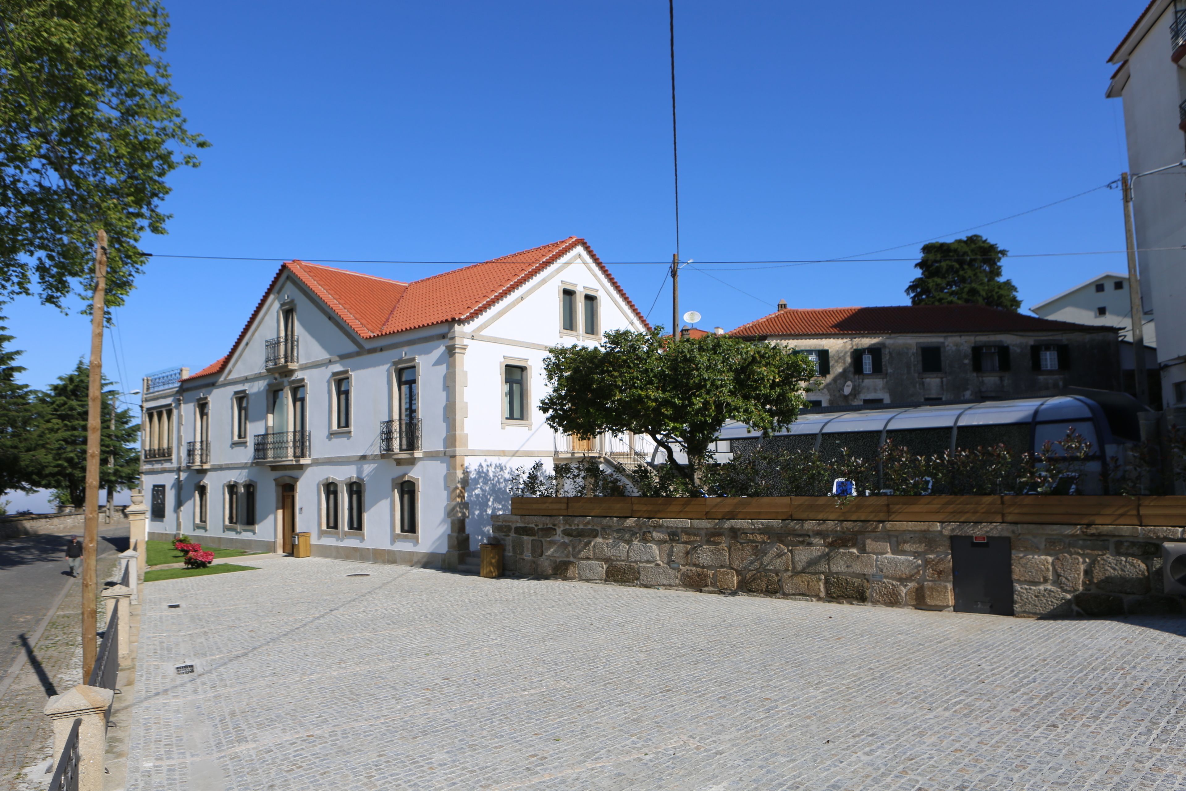 A historic building with a red-tiled roof, stone wall, and a paved courtyard.