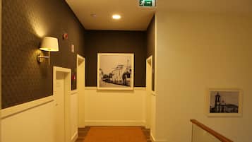 A hallway with a patterned wall, a framed photograph, and a lamp.