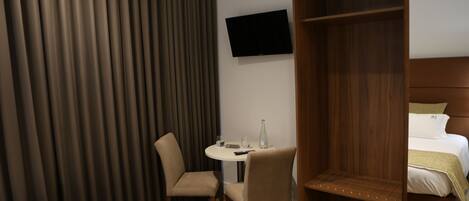 Ein Hotelzimmer mit Bett, Wandfernseher, kleinem runden Tisch mit Stuhl und Holzschrank.