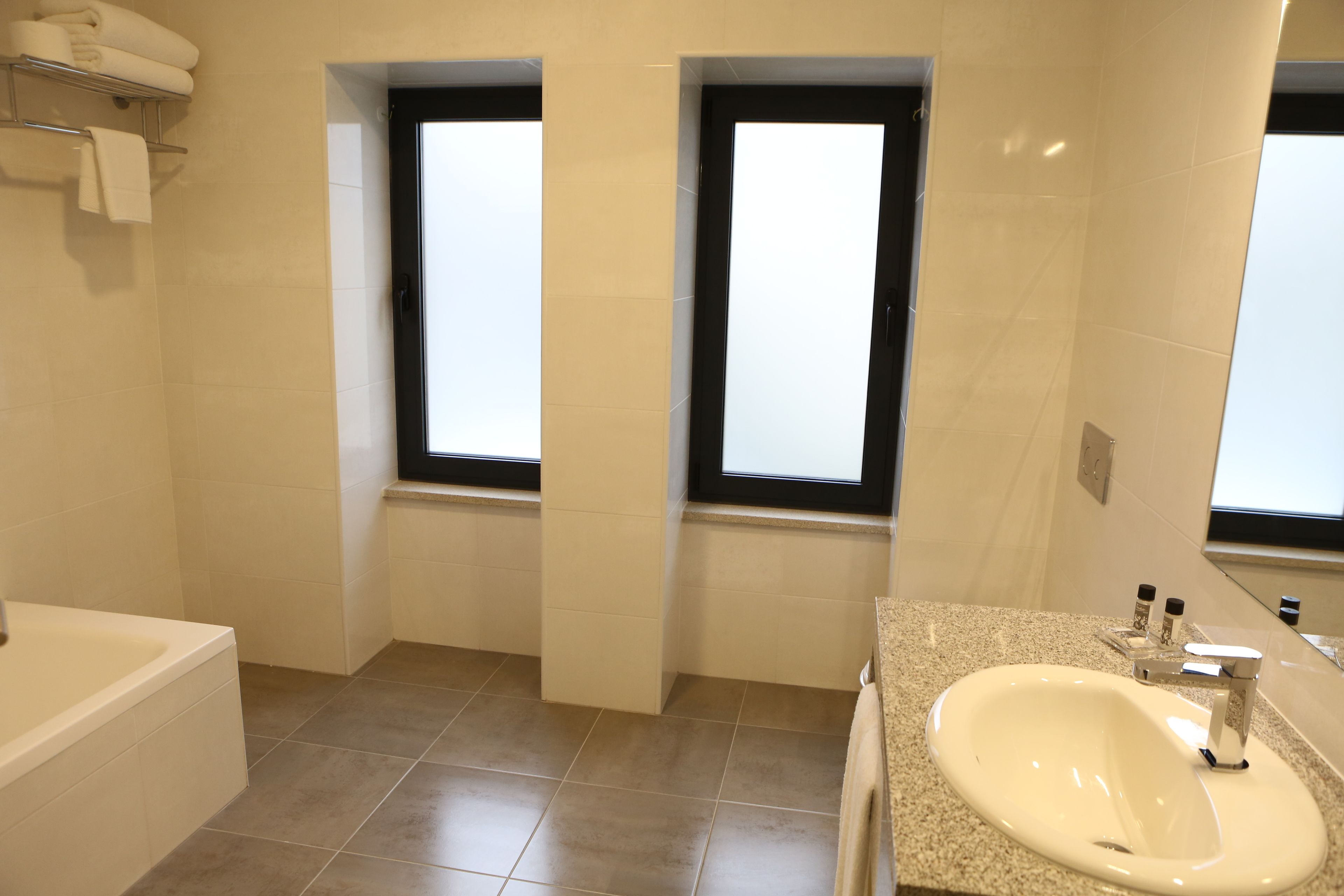 Un baño moderno con bañera, lavamanos y dos ventanas.