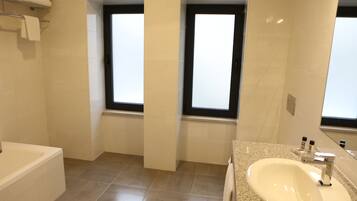 Un baño moderno con bañera, lavamanos y dos ventanas.