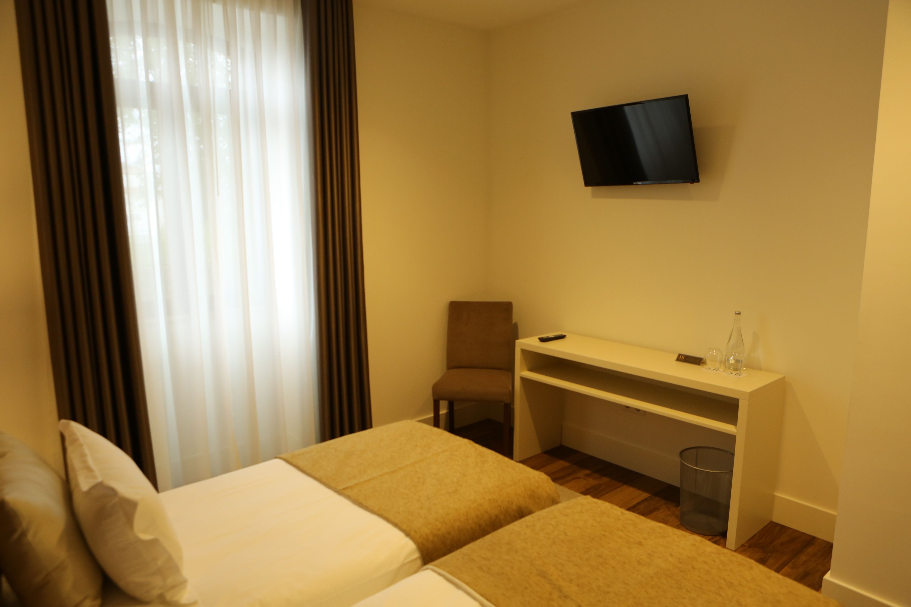 Ein Hotelzimmer mit zwei Betten, einem Schreibtisch, einem Stuhl, einem Fernseher und einem Papierkorb.