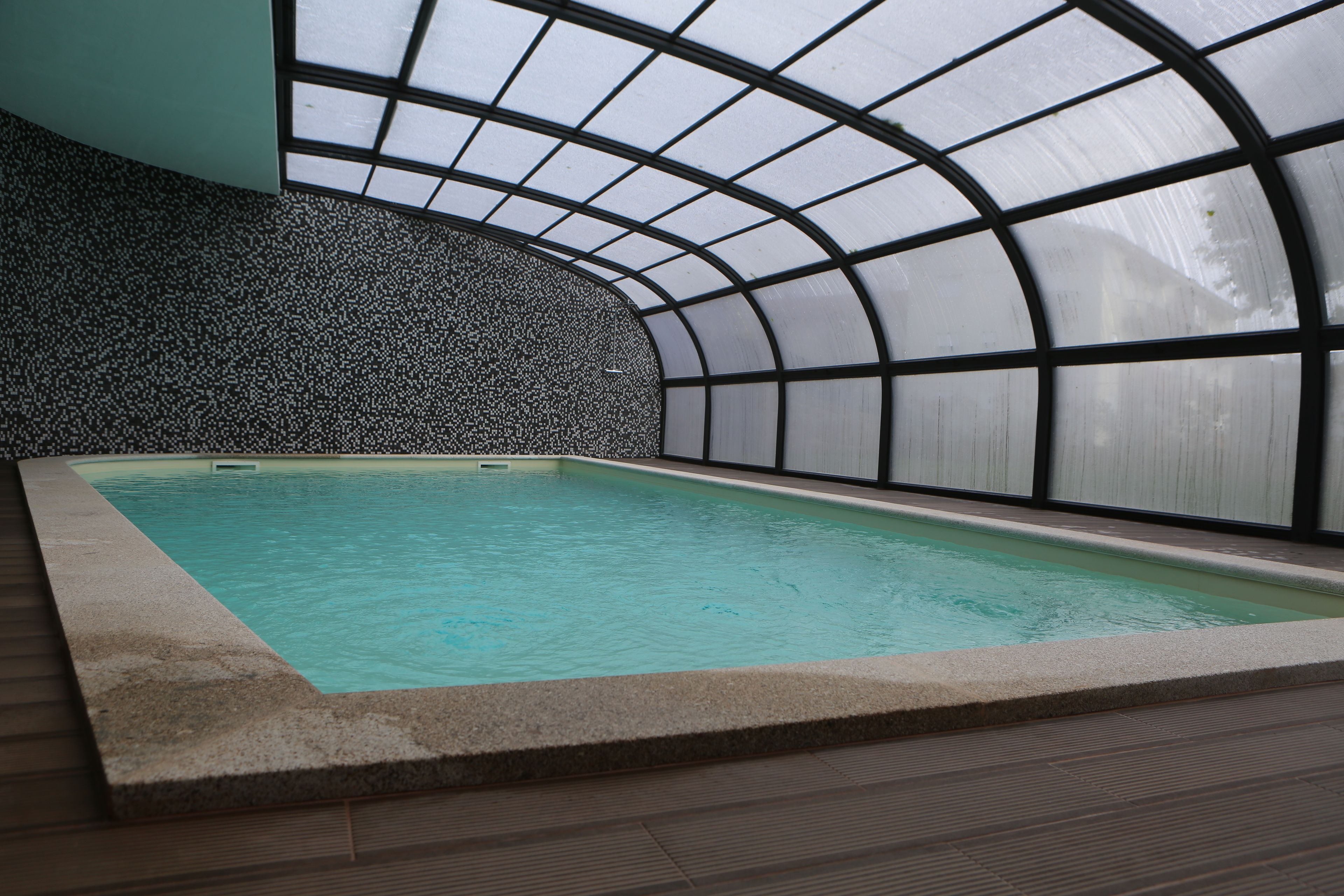 Piscina interna com teto curvo e parede com textura de pedrinhas.
