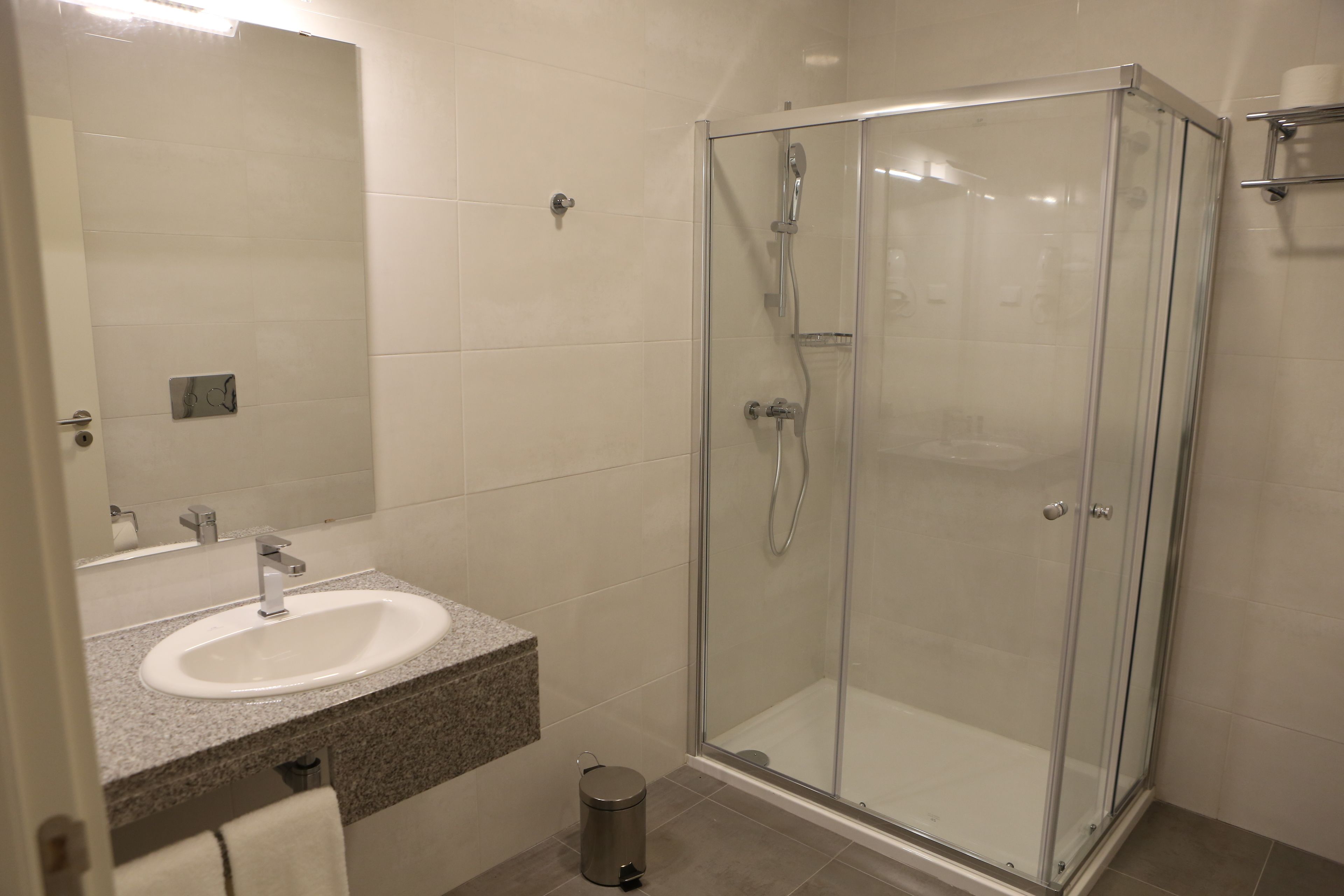 Ein modernes Badezimmer mit einer Duschkabine aus Glas, einem Waschbecken mit Granitplatte und einem Spiegel darüber.