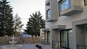A modern building with a stone wall, a fountain, and tall trees. - Hotel Solar do Rebolo (Oliveira do Hospital)