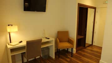 Habitación de hotel con escritorio, silla, televisor, lámpara y suelo de madera.