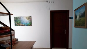 A room with a wooden table, a bookshelf with books, a door, and two framed paintings on the wall. - Bolero Apart Hotel (Bodrum)