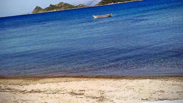 A boat on calm blue water with a sandy beach and a mountain in the background. - Bolero Apart Hotel (Bodrum)