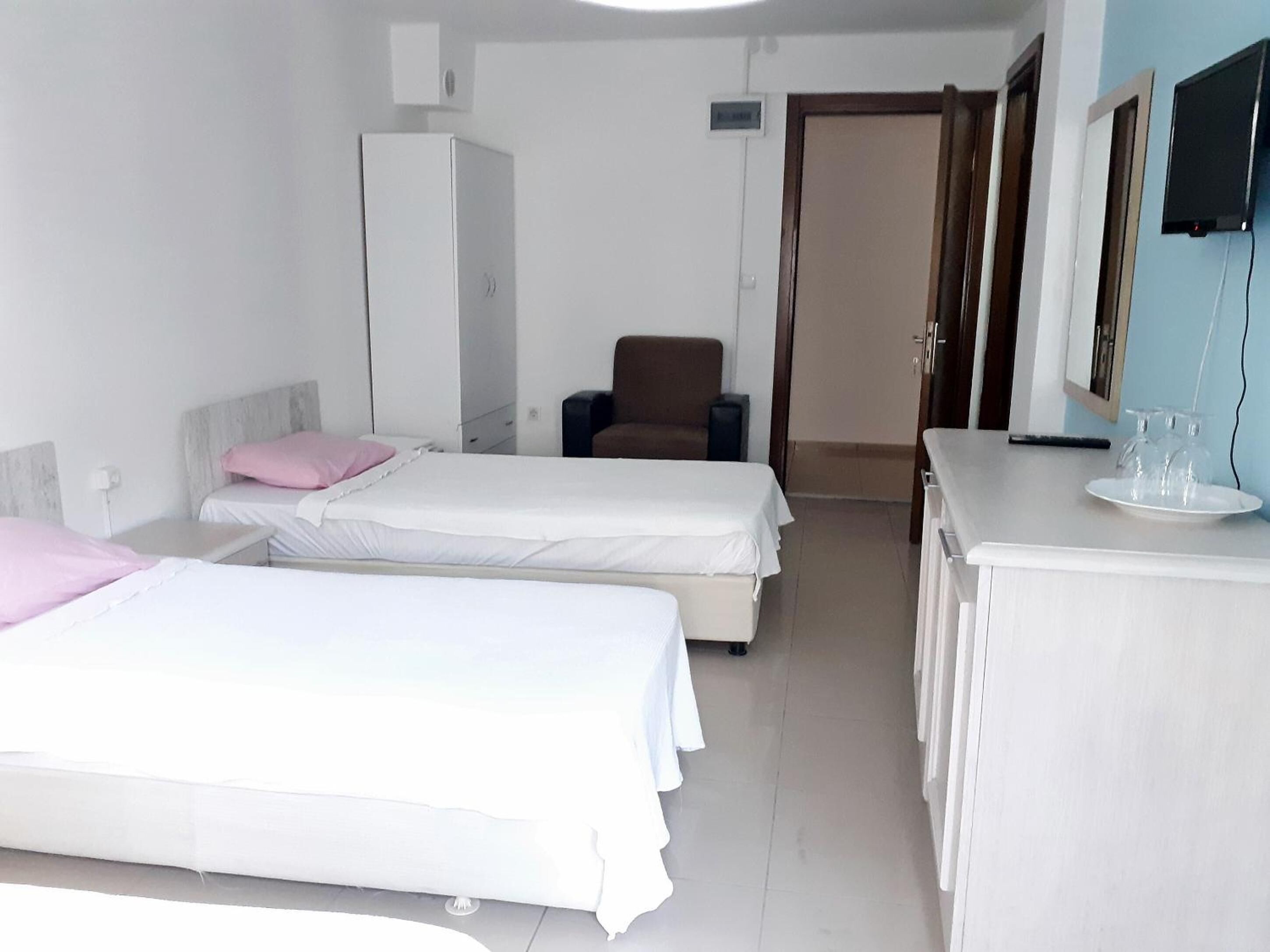 A hotel room with two single beds, a desk with a chair, a wardrobe, and a television on the wall.
