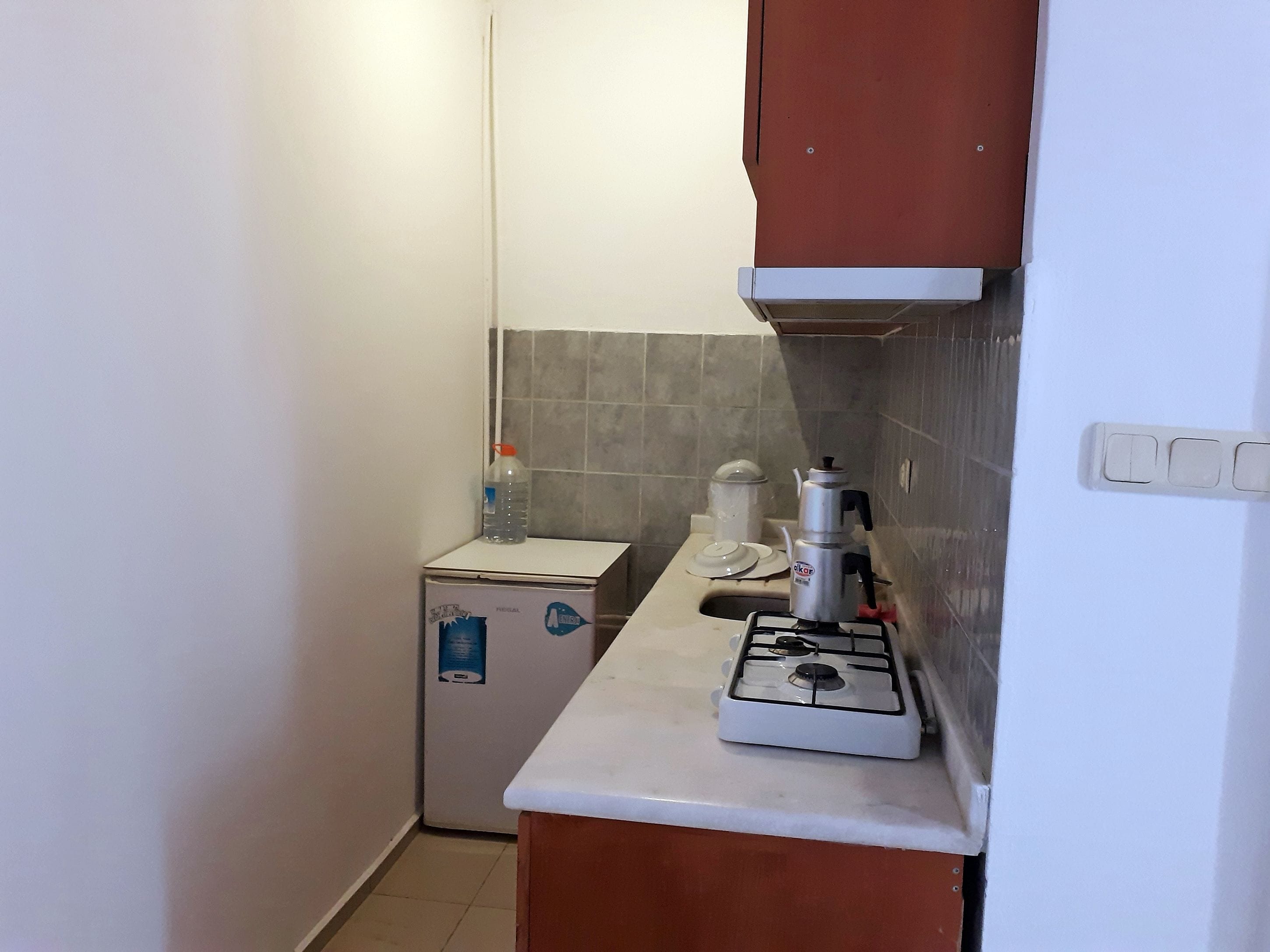 A compact kitchen with a gas stove, a small refrigerator, and a water dispenser.