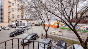 Un estacionamiento con varios coches, un árbol y un mural colorido al fondo.