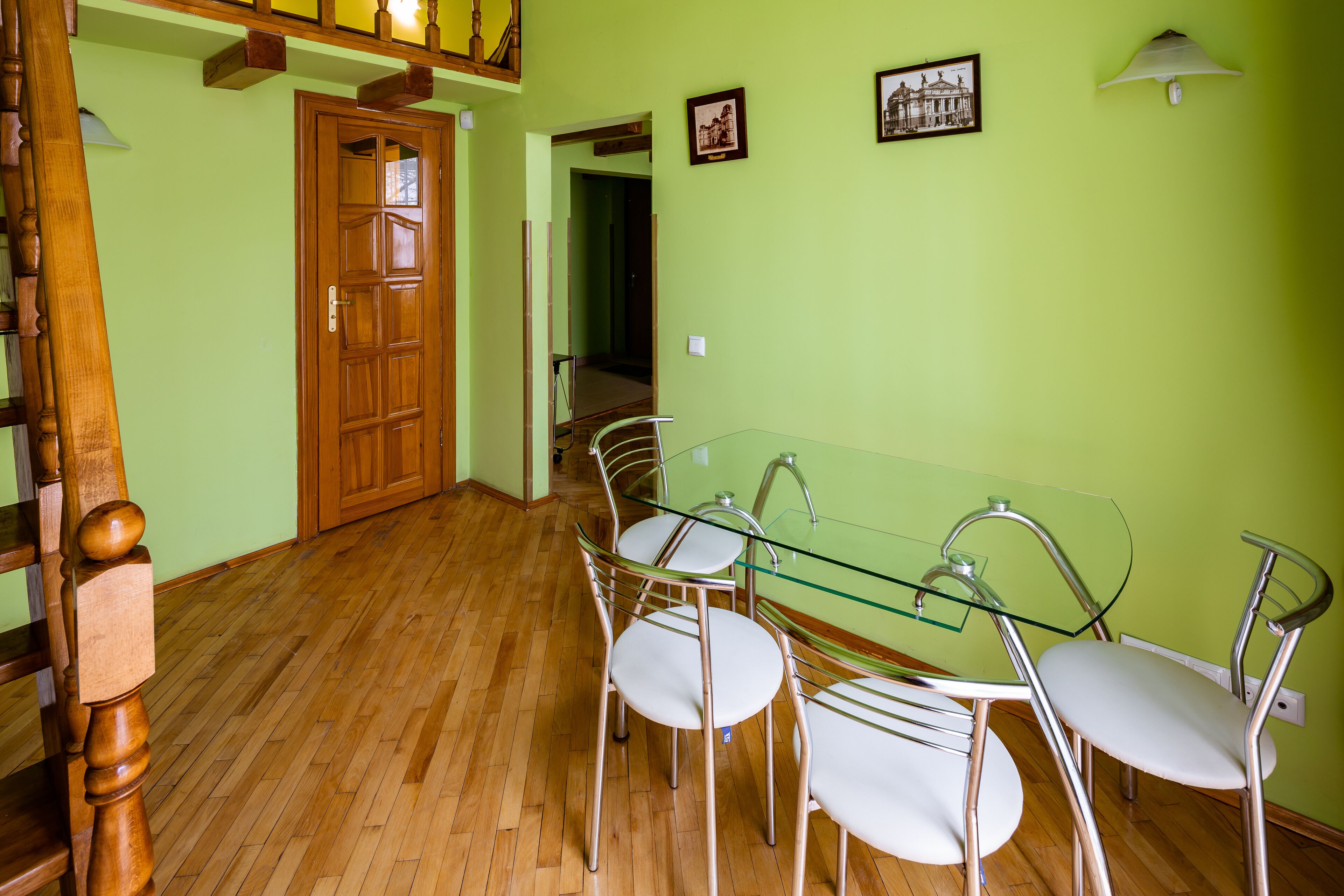 Un comedor con mesa de vidrio, sillas de metal, una puerta de madera y una escalera.