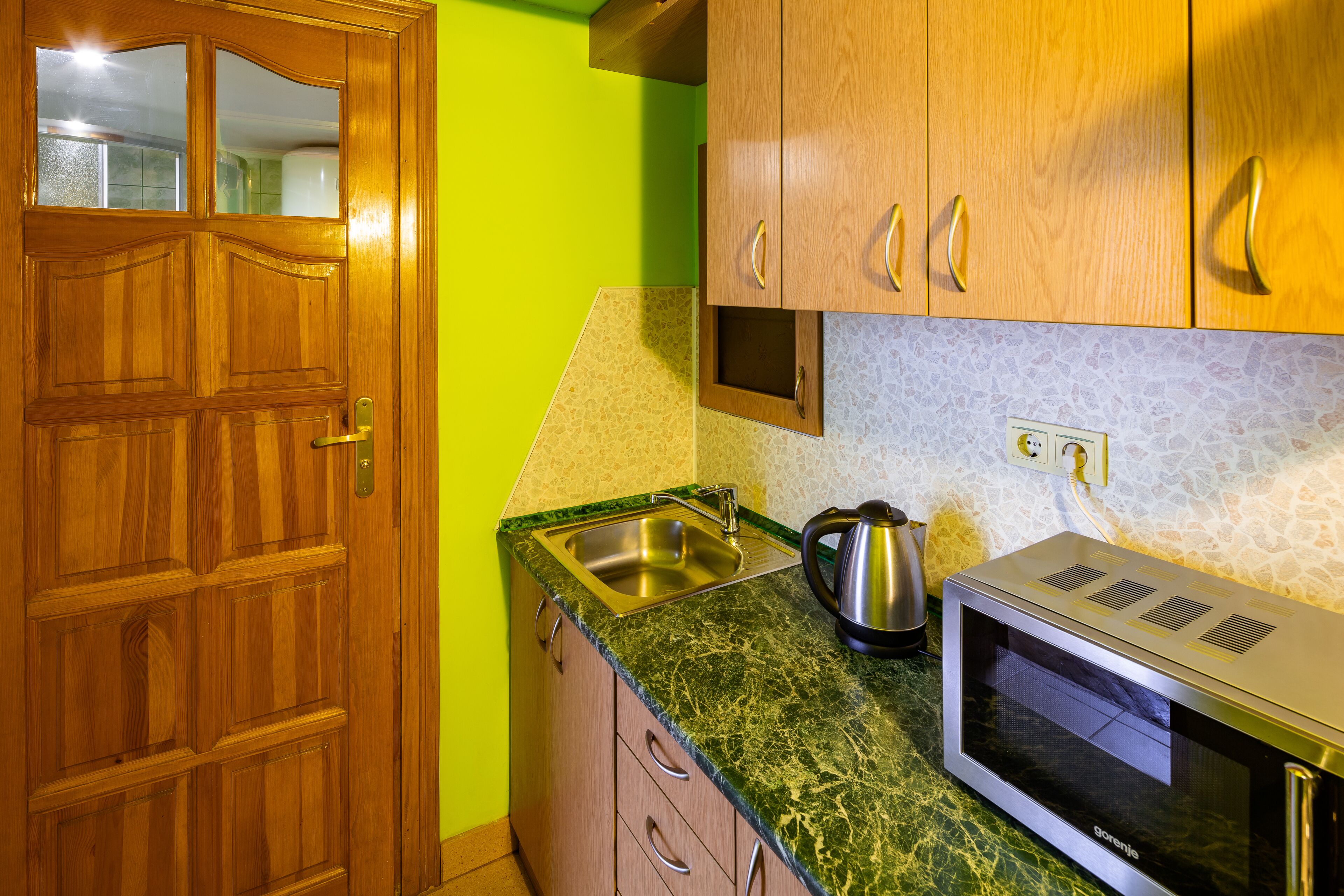 Una cocina con armarios de madera, encimera verde, pileta de acero inoxidable y un microondas.