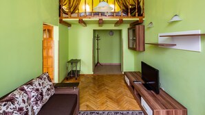Una habitación con suelo de espiga, un sofá, un televisor y un techo de madera con cortinas.