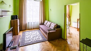 Una habitación con sofá, televisión, alfombra y suelo de madera.