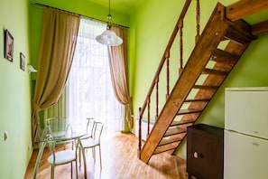 A room with a dining table, chairs, a staircase, and a refrigerator.