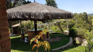 Ein mit Stroh gedecktes Pavillon in einem Garten mit Backsteinbauten und Grünpflanzen.