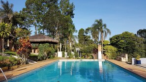 Piscina rodeada por vegetação exuberante e uma construção com telhado de palha.