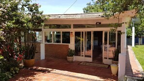 A covered patio area with a brick floor, potted plants, and a glass door entrance leading inside. - Sítio Brasiliano em Mairinque (Mairinque)