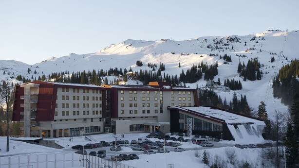 Een hotel met meerdere verdiepingen, een parkeerplaats en een bergachtige achtergrond.